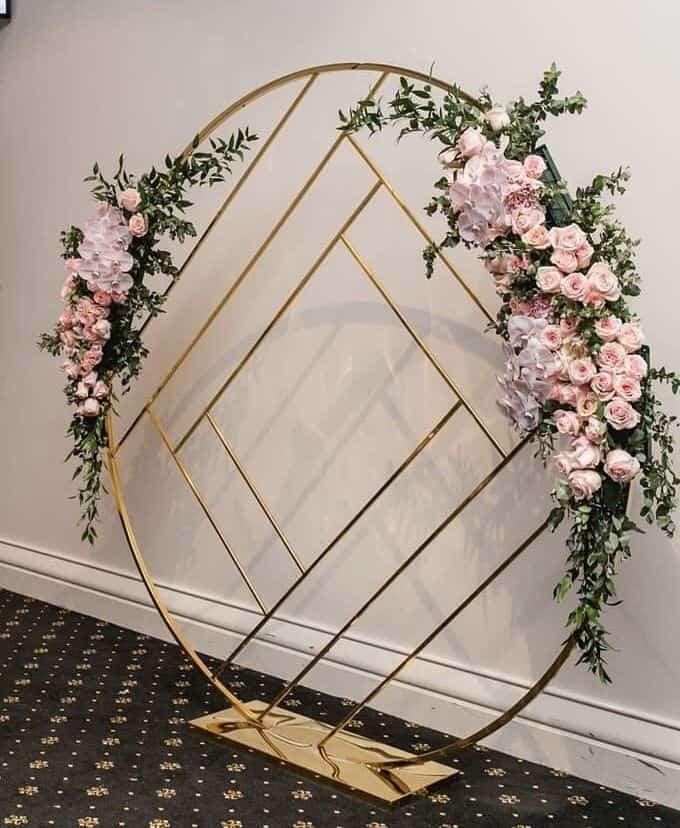 Gold and pink wedding arch adorned with flowers available for decoration hire.