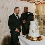 Two men in suits standing next to a cake.