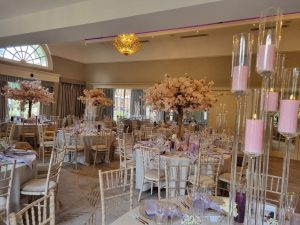 A wedding reception with pink flowers and candles in a large room.