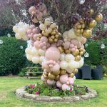 A pink and gold balloon tree in a garden.