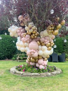 A pink and gold balloon tree in a garden.
