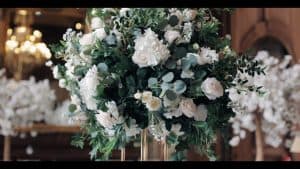 An arrangement of white flowers and greenery in a tall vase.