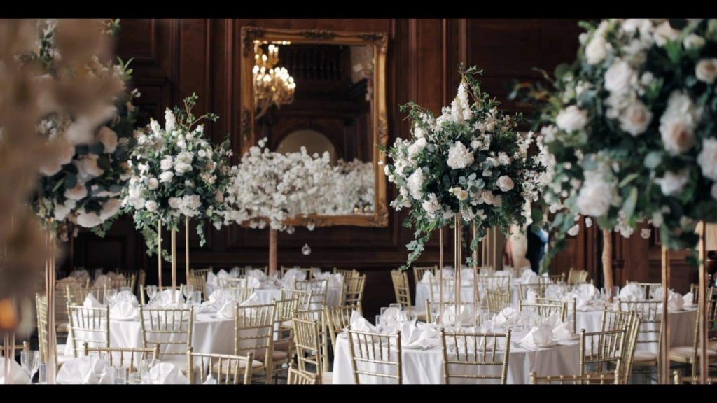 A large ballroom with white tables and white flowers.